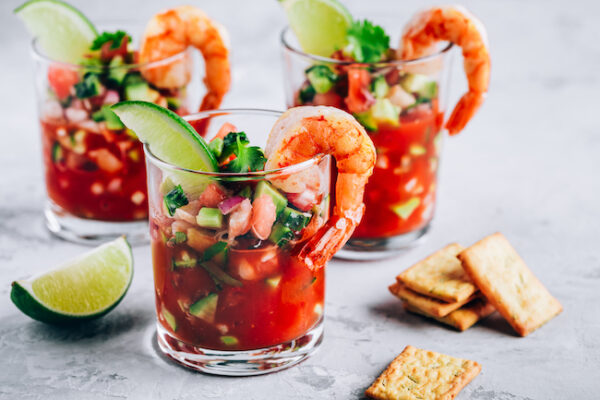Refreshing Mexican Shrimp Cocktail with lime in glass on gray stone background, copy space.