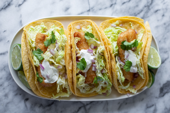 Three fish tacos on soft corn tortillas with cabbage, red onion, cilantro and lime.